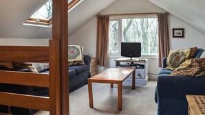 A cozy attic room with a wooden table, two sofas, a TV, and a window with curtains.