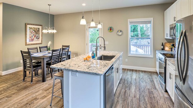 A modern kitchen with a granite countertop, stainless steel appliances, and a dining area with wooden chairs and a table. - Modern Candler Home w/ Deck & Yard! (Candler)
