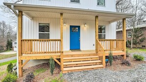 A two-story house with a wooden porch, a blue door, and a gravel driveway. - Modern Candler Home w/ Deck & Yard! (Candler)