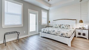 Une chambre à coucher comprenant un lit, une table de chevet, un banc, un ventilateur de plafond et une fenêtre avec des stores.