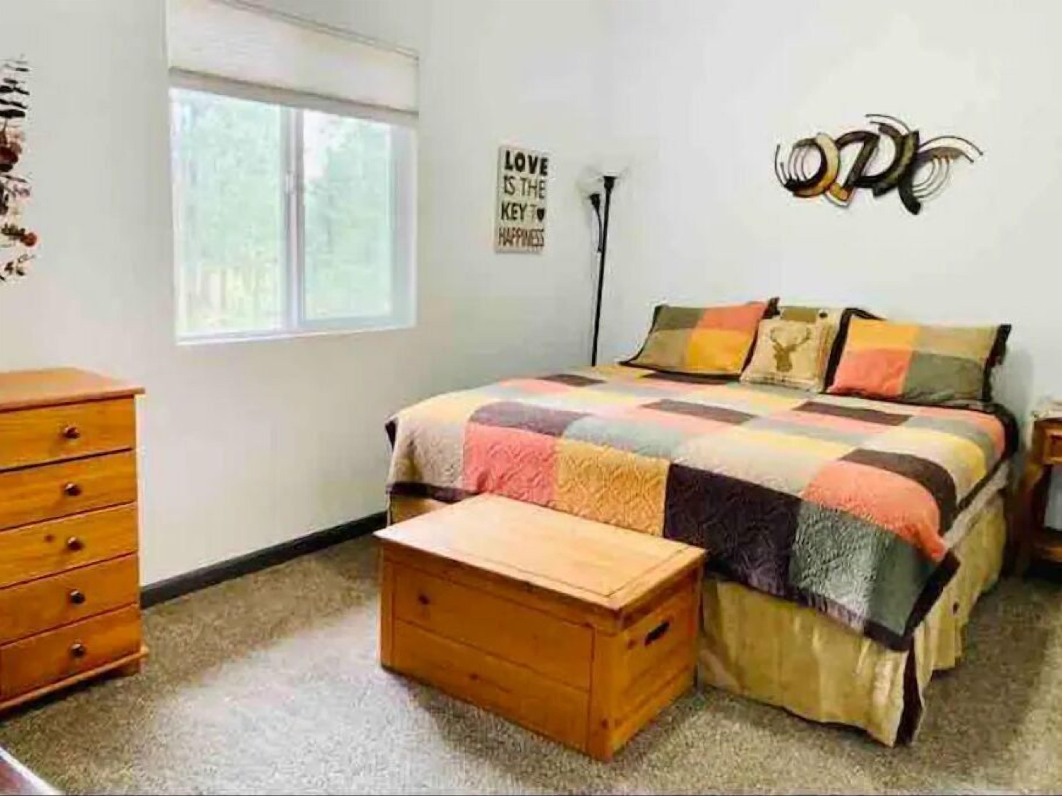 A bedroom with a bed, a wooden chest, a dresser, and a wall with a motivational quote.