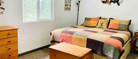 A bedroom with a bed, a wooden chest, a dresser, and a wall with a motivational quote.