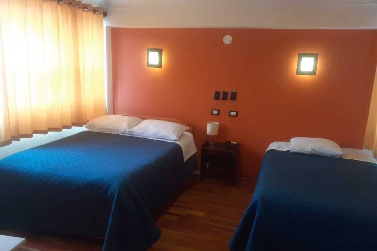 A room with two beds, wooden flooring, orange walls, and two wall-mounted lights.