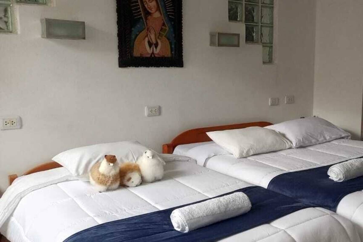 A double bed with white and blue bedding, two pillows, and two rolled towels.