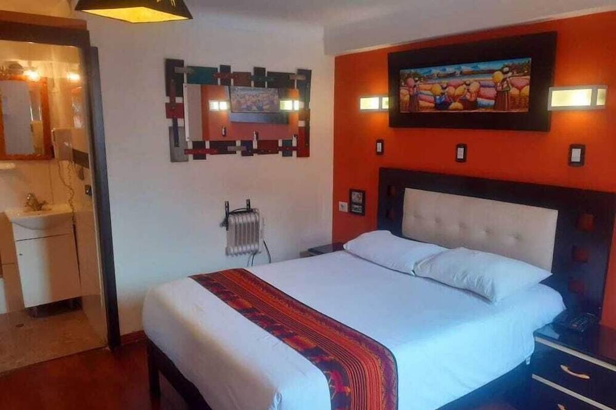 A hotel room with a bed, a dresser, a radiator, and a wall-mounted artwork.