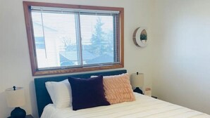 A bedroom with a bed, a nightstand, a lamp, a window, and a wall clock. - Bay Street Unit 3 · Charming & Cozy APT-Free Parking (Appleton)
