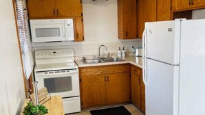 A compact kitchen with wooden cabinets, a white refrigerator, a microwave, a stove, and a sink. - Bay Street Unit 3 · Charming & Cozy APT-Free Parking (Appleton)
