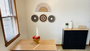 A dining area with a wooden table and bench, a decorative wall piece above, and a small cabinet with a sign. - Bay Street Unit 3 · Charming & Cozy APT-Free Parking (Appleton)