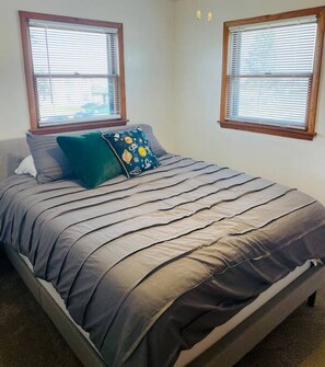 A bedroom with a bed, two windows, and a wall-mounted light fixture. - Bay Street Unit 3 · Charming & Cozy APT-Free Parking (Appleton)