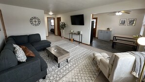 A living room with a sofa, coffee table, and armchair, a TV mounted on the wall, and a kitchen area in the background. - Chic & Cozy APT-Self Check-In (Appleton)