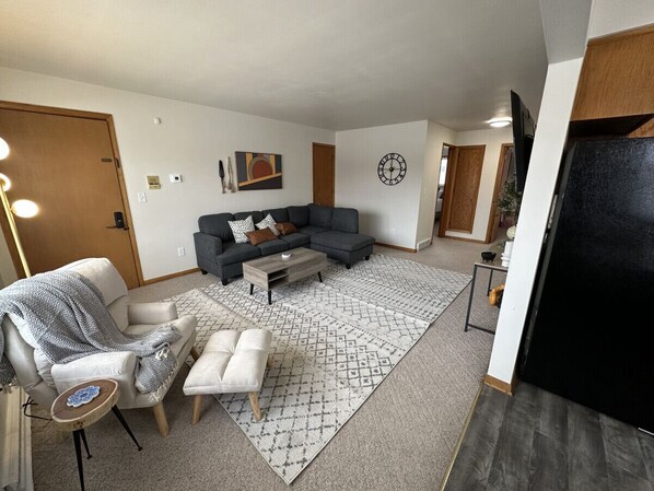A living room with a sectional sofa, a coffee table, a patterned rug, and a side table with a decorative item.