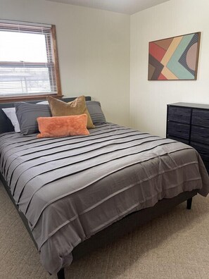 A bedroom with a bed, pillows, a dresser, and a wall art piece.