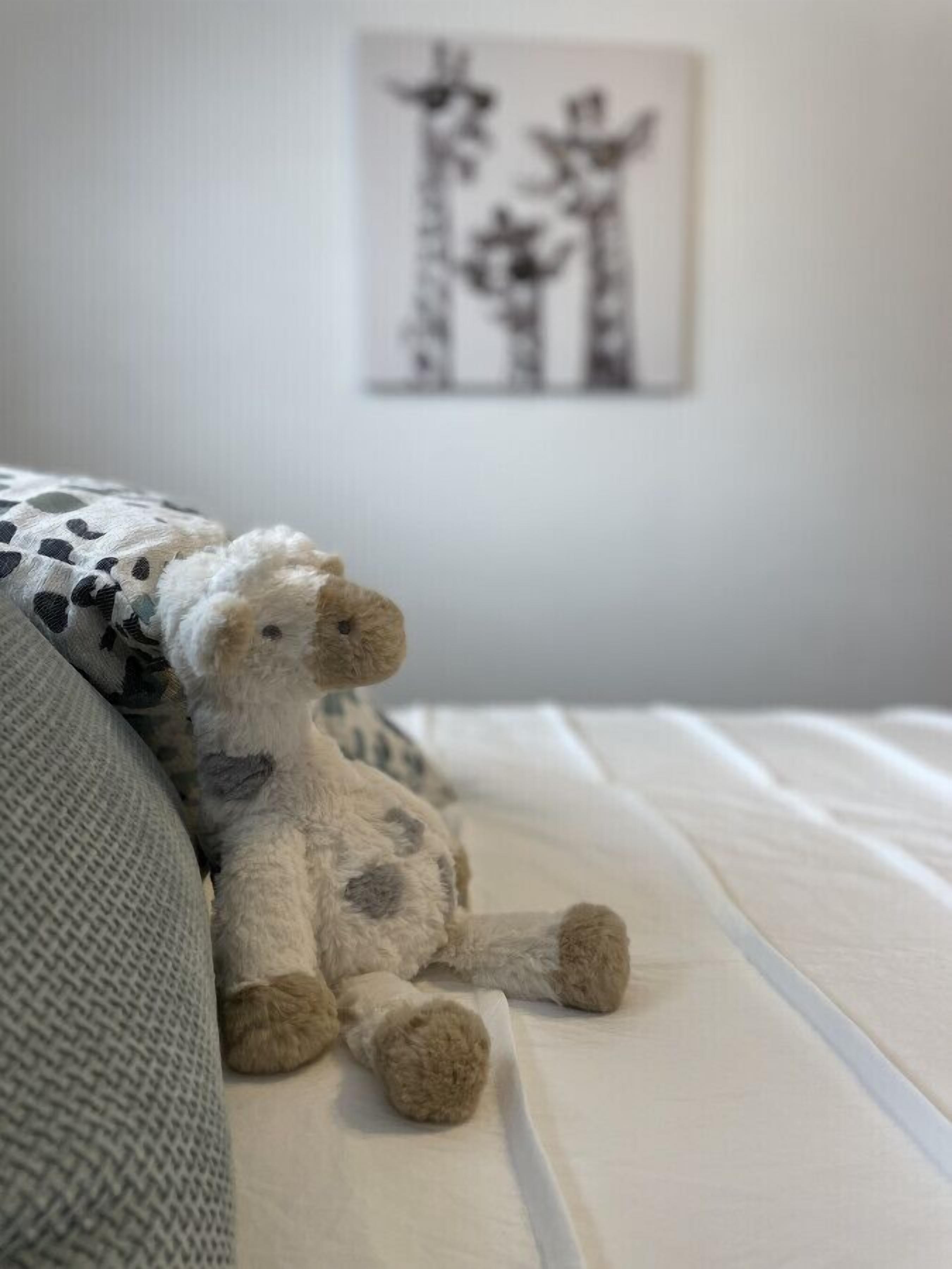 Un lit avec une couette blanche et un ours en peluche à motifs pointillés.