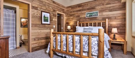 A wooden-paneled bedroom with a wooden bed, a ceiling fan, and a nightstand with a lamp.