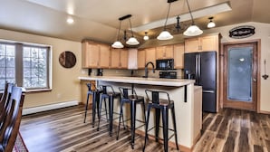 Una cocina con armarios de madera, un refrigerador negro, un microondas y una zona de bar con taburetes.