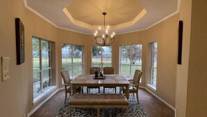 A dining area with a large table, chairs, a bench, a chandelier, and large windows with a view of a grassy area. - Farmhouse & Ranch style living for your vacay with pond, gazebo, trellis, pool.. (Farmersville)