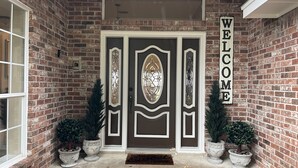 A brick house entrance with a double door, a welcome sign, and potted plants. - Farmhouse & Ranch style living for your vacay with pond, gazebo, trellis, pool.. (Farmersville)