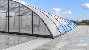 Una estructura de invernadero grande y curvada con techo y paredes transparentes, ubicada sobre un piso de baldosas.