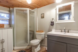 Une salle de bain avec une douche à parois de verre, des toilettes, un lavabo avec un miroir et une fenêtre.