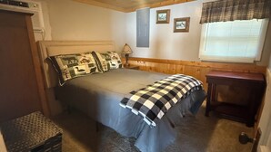 Un dormitorio con cama, mesita de noche, lámpara, ventana con persianas e iluminación en el techo.