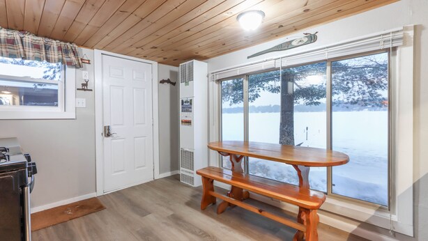 Una cocina con una mesa y banco de madera, una ventana que ofrece vistas a un paisaje nevado y una puerta blanca.