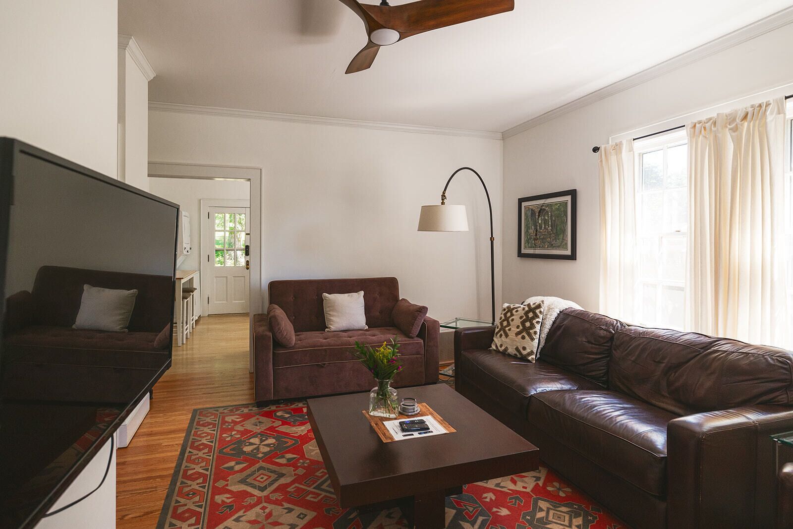 A living room with a brown sofa, a brown armchair, a coffee table with a vase of flowers, a floor lamp, and a television.