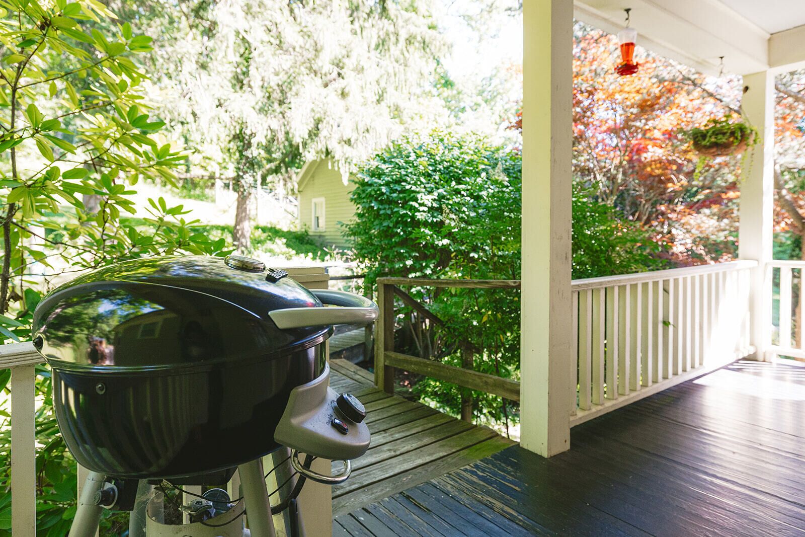 A covered outdoor area with a barbecue grill, wooden deck, and a white railing.