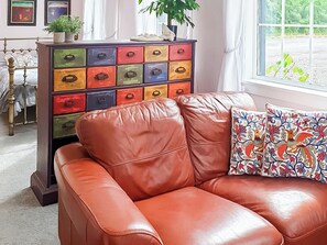 A room with a brown leather sofa, a colorful chest of drawers, and a window with a view of greenery.