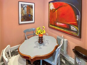 A dining area with a round table, chairs, a vase with flowers, a framed painting, and a radiator. - Hobgoblin Apartment - UK42205 (Glendaruel)