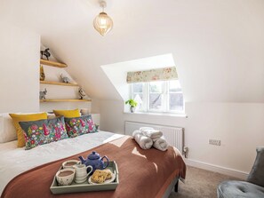 A bedroom with a bed, a window, a radiator, a shelf with decorative items, and a tray with tea and biscuits.