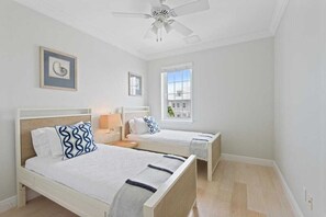 A bedroom with two beds, a ceiling fan, a window, and artwork on the wall.