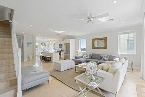 A spacious living room with a grey sofa, a glass coffee table, and a white ottoman.