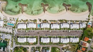 An aerial view of a resort with multiple white-roofed buildings, a beach, and a parking area.