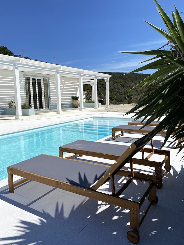 A pool area with lounge chairs and a white building with glass doors.
