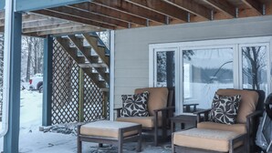 A covered outdoor seating area with two chairs and a table, a wooden staircase, and a view of a snowy landscape.