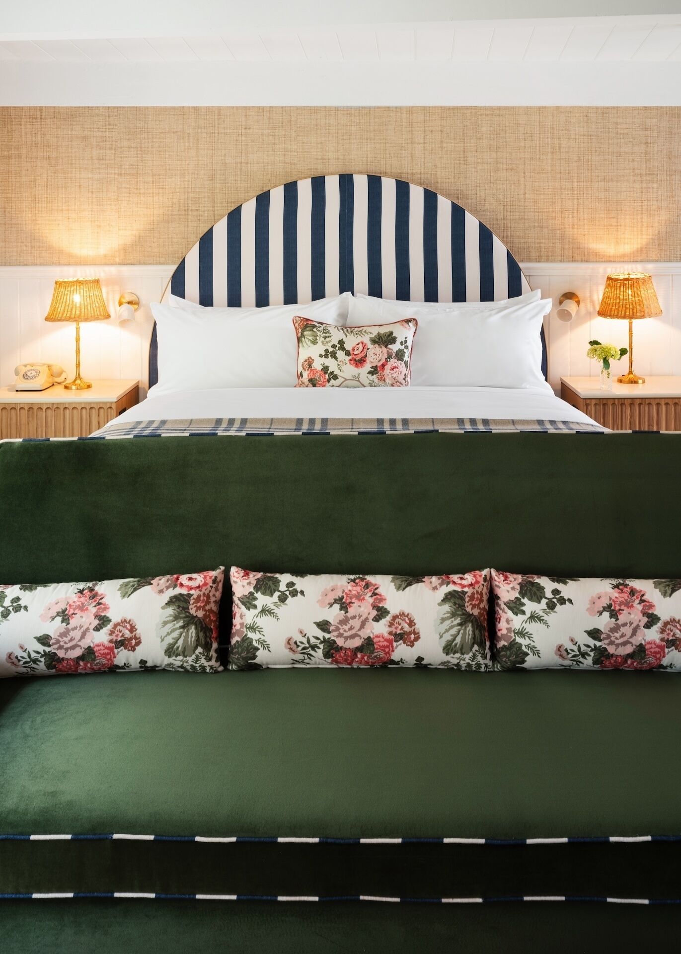 A bed with a striped headboard, floral pillows, and green bedding.