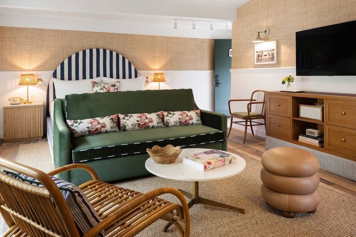 A cozy living room with a green sofa, wicker chairs, a round ottoman, and a television on a wooden cabinet.