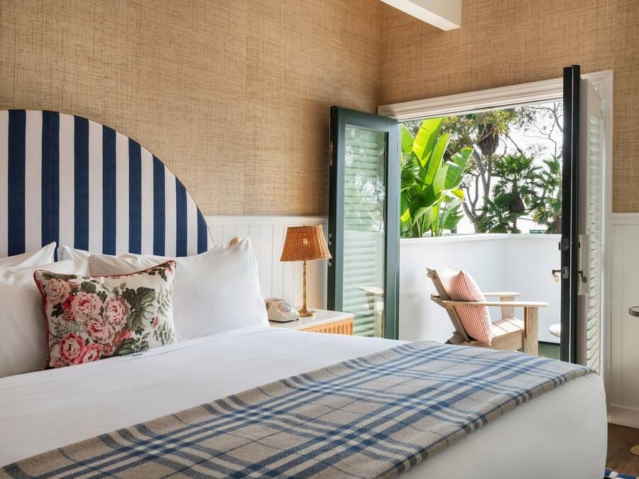 Un dormitorio con una cama, una mesita de noche, una lámpara y vistas a un balcón con plantas.