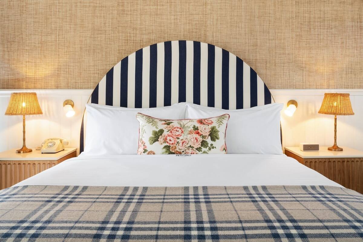 A neatly made bed with a striped headboard, white pillows, and a floral accent pillow. There are two bedside tables with lamps and a telephone on one.