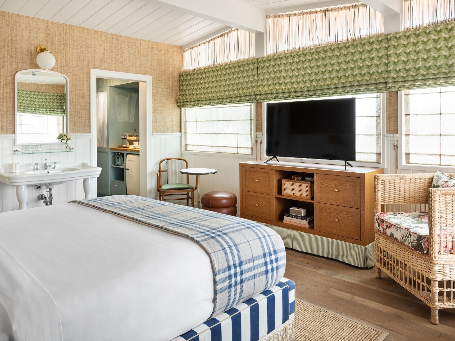 Un dormitorio con cama, televisor, cómoda, silla y ventana con cortinas.