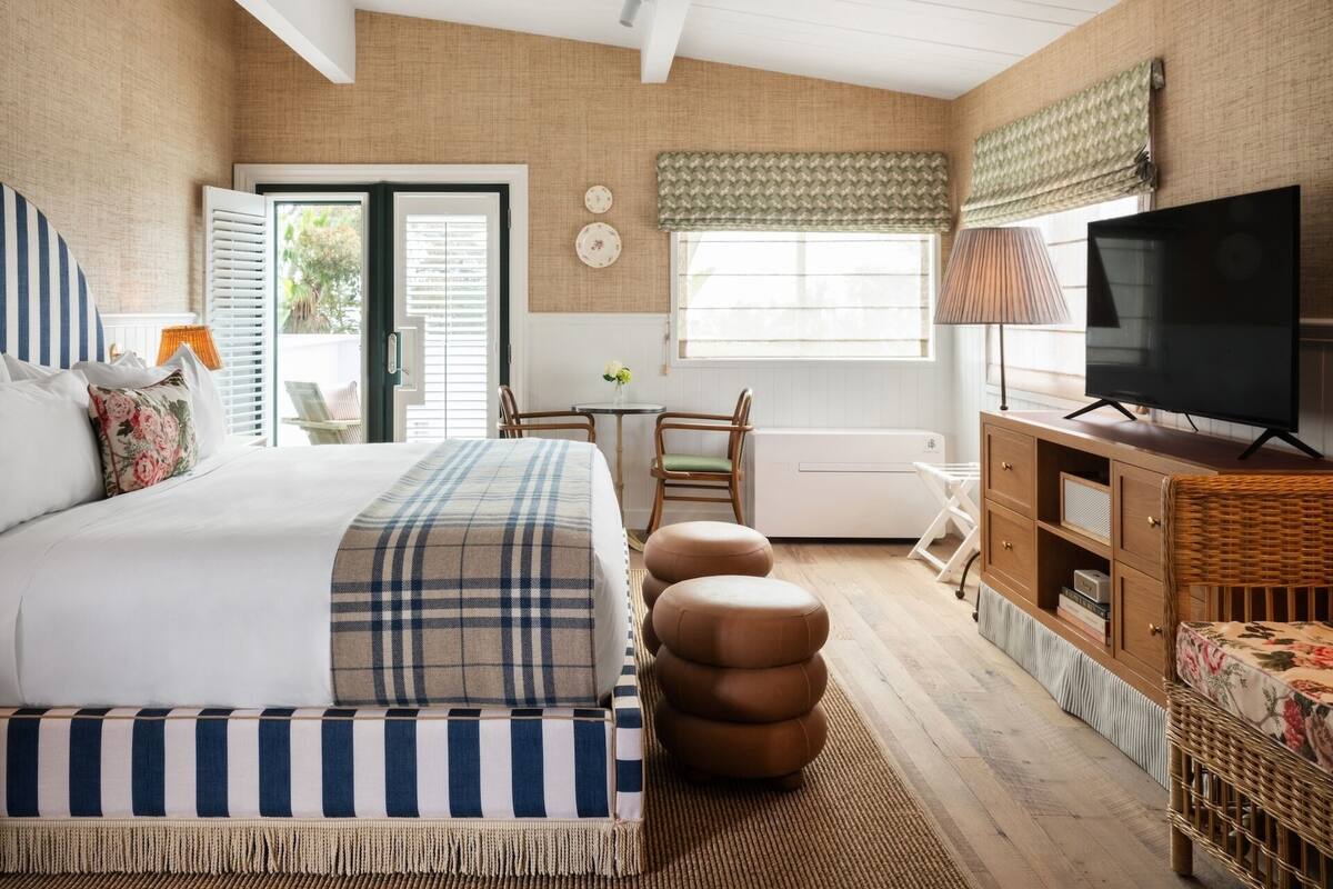 A bedroom with a bed, a television, a dining table, and a wicker chair.
