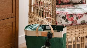 A wicker chair with floral cushions, a green tote bag with a logo, and a striped cushion on a wooden floor.