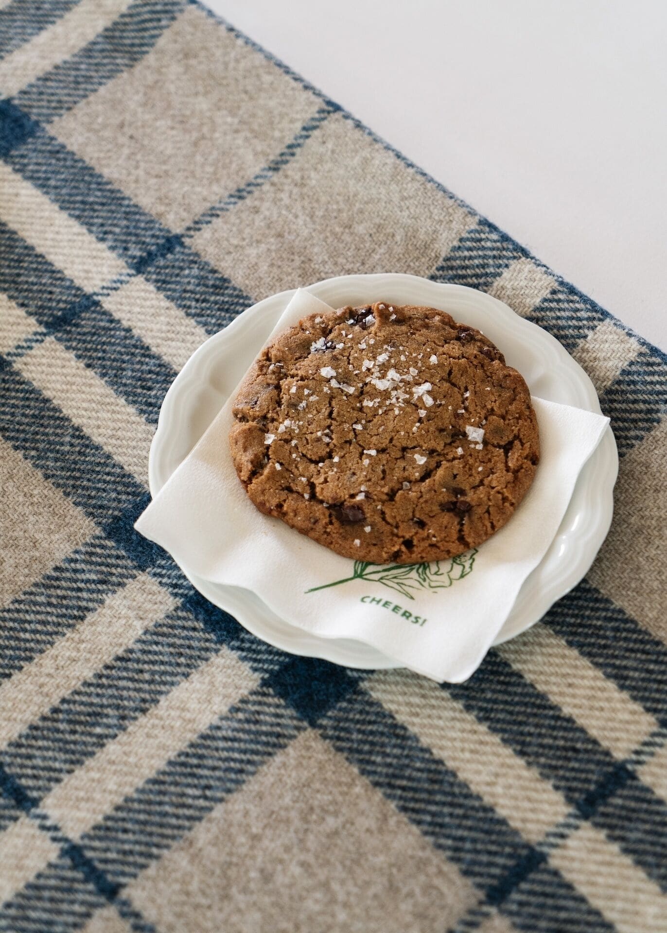 A cookie on a white plate with a blue and beige checkered tablecloth.