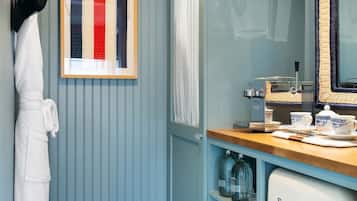 Un baño con piso de cuadros, una bata blanca colgada, un cuadro enmarcado, un espejo y un lavamanos de estilo vintage con un refrigerador Smeg.