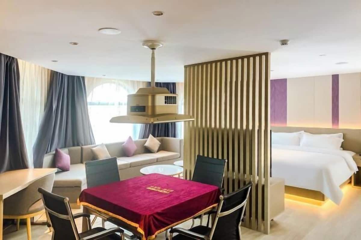 A hotel room with a dining table, a sofa, a bed, and a decorative partition.