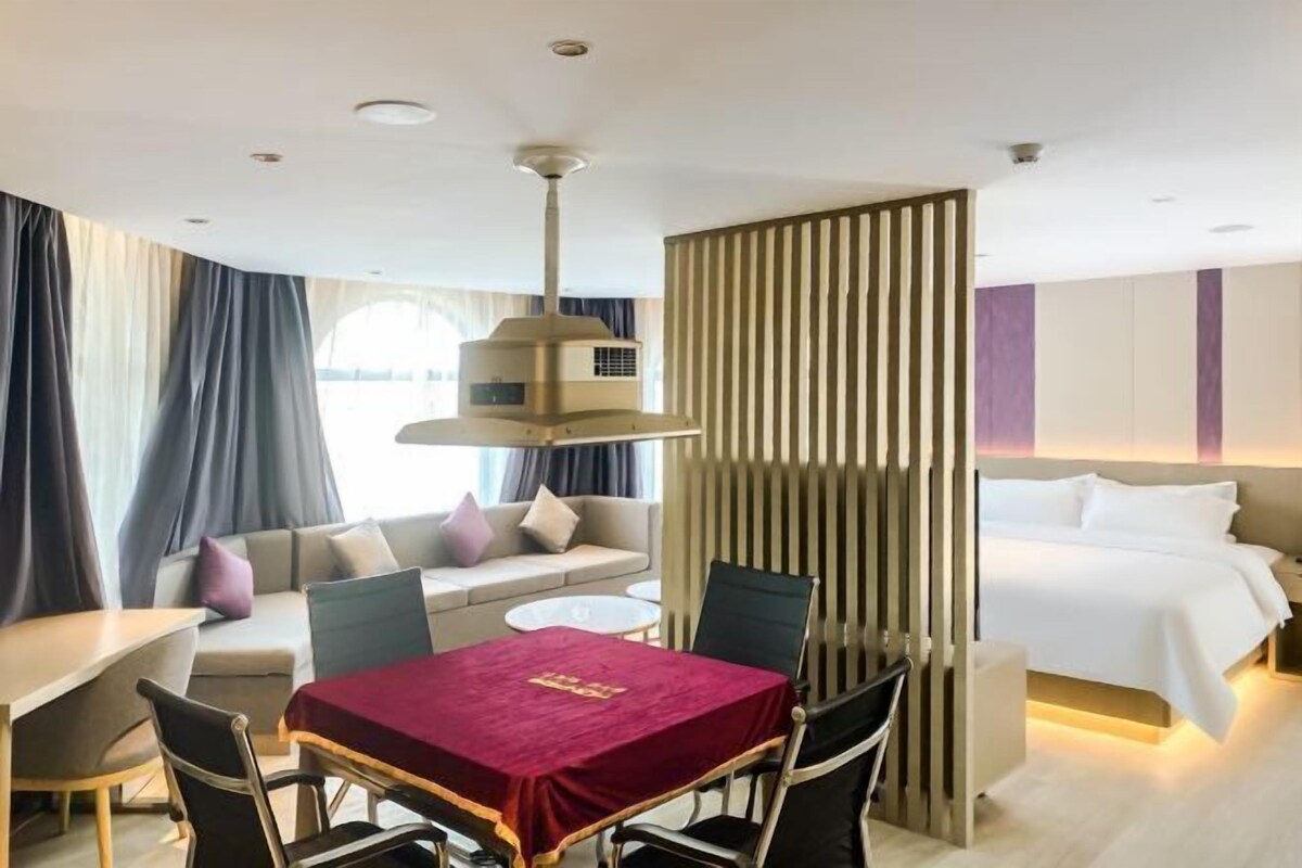 A hotel room with a dining table, a sofa, a bed, and a partition wall.