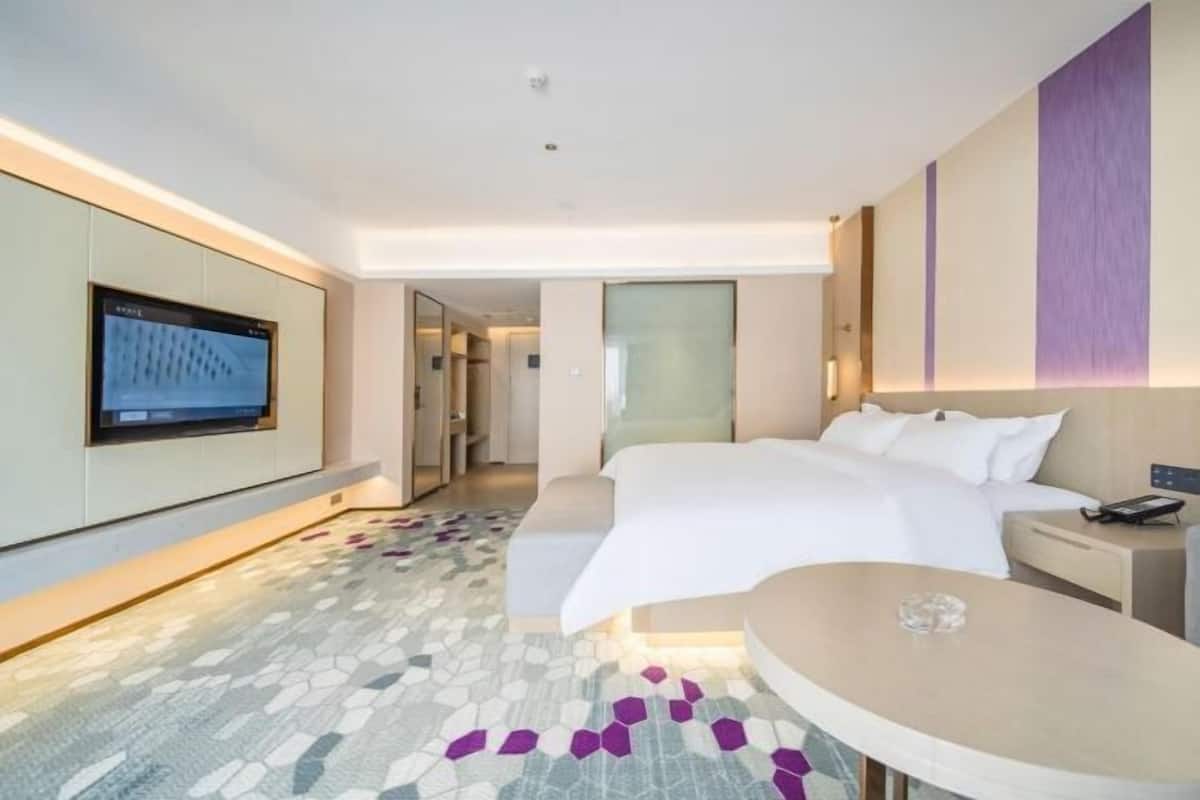 A modern hotel room with a large bed, a TV mounted on the wall, and a small round table.