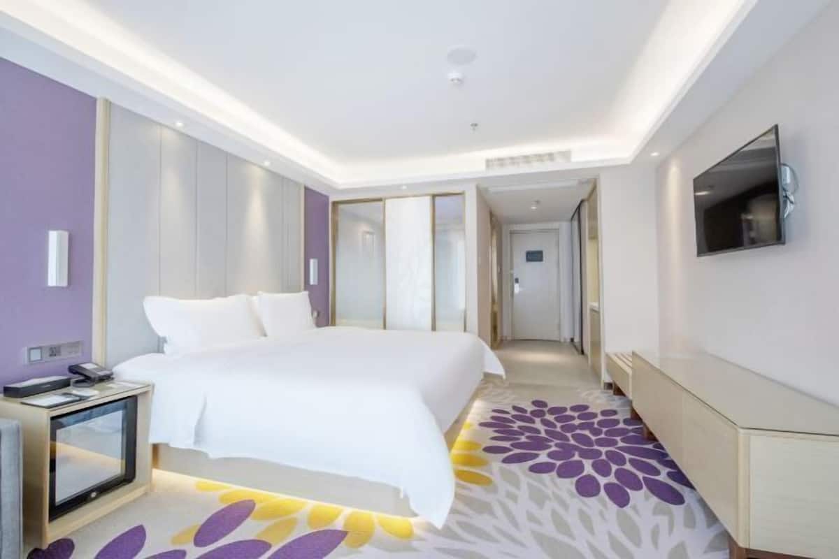 A modern hotel room with a large bed, a bedside table, a TV, and a patterned carpet.
