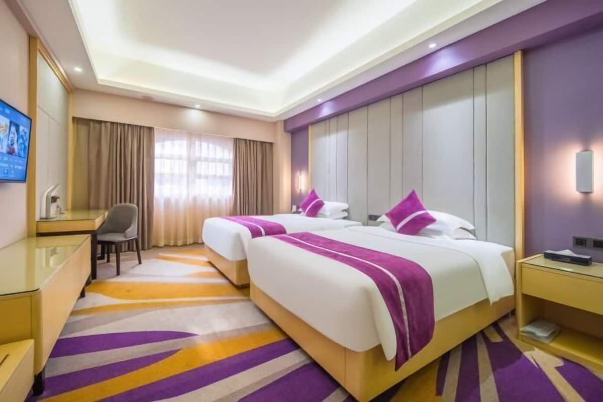 A hotel room with two beds, a desk, and a television.