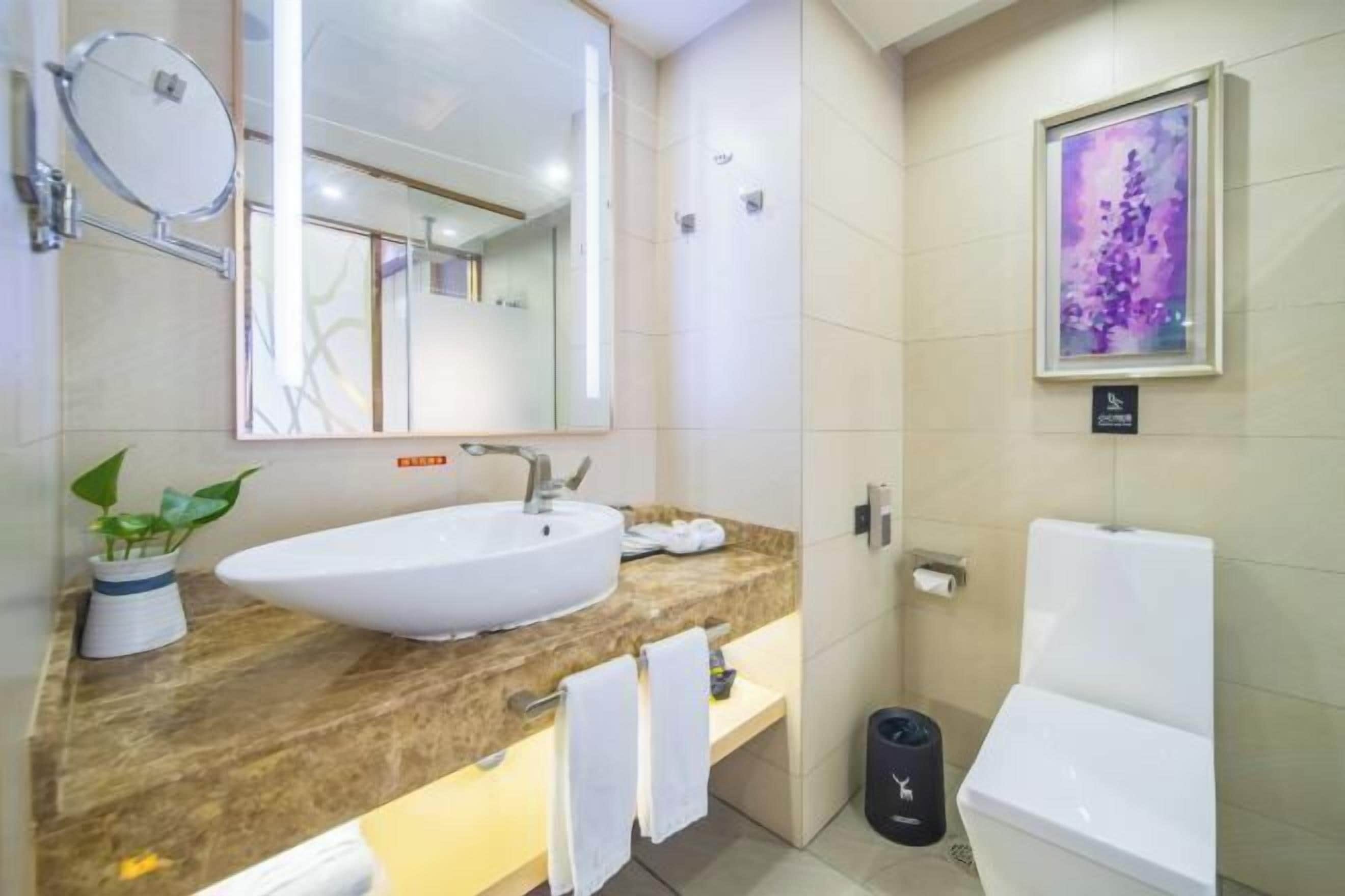 A modern bathroom with a large sink, a mirror, a toilet, and a framed artwork on the wall.